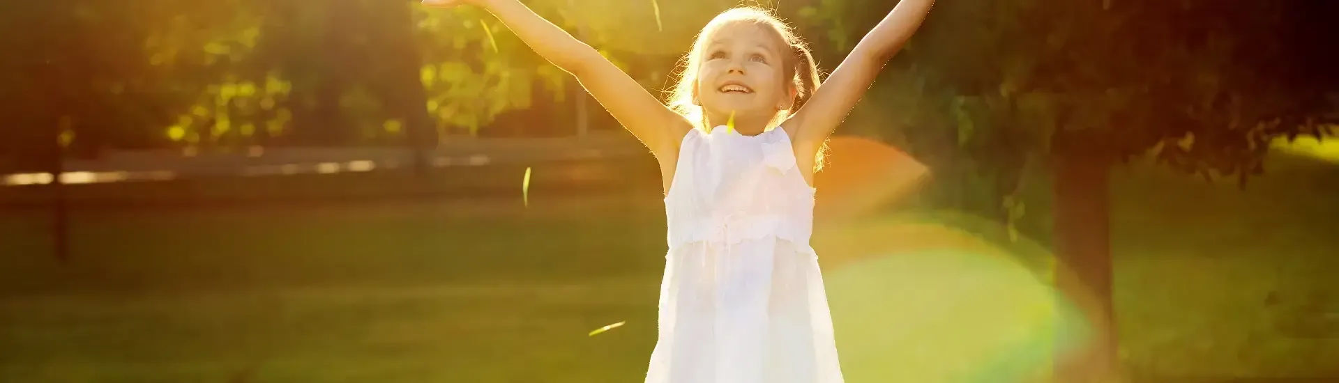 A little girl in a white dress holding her arms up in the air