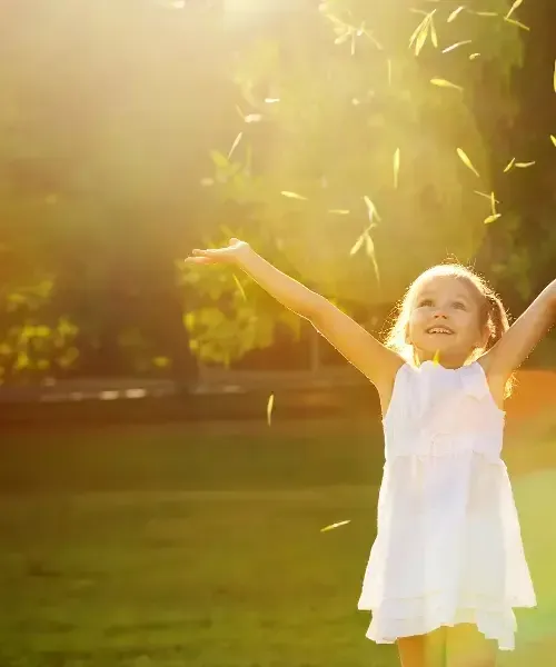 A little girl in a white dress holding her arms up in the air