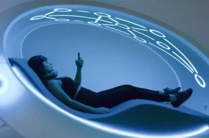 A woman laying in a biohacking orb with a cell phone in her hand